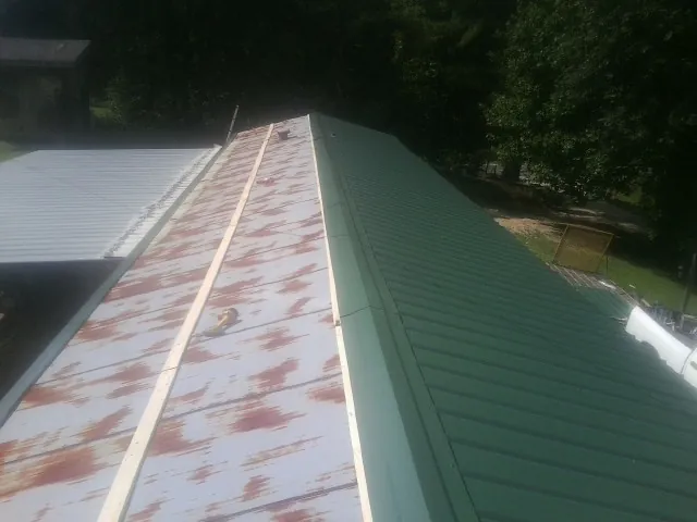 Old rusted panels beside newly installed green metal roofing — Wind Damage Roof Repair by Roofing Brothers in Wilton