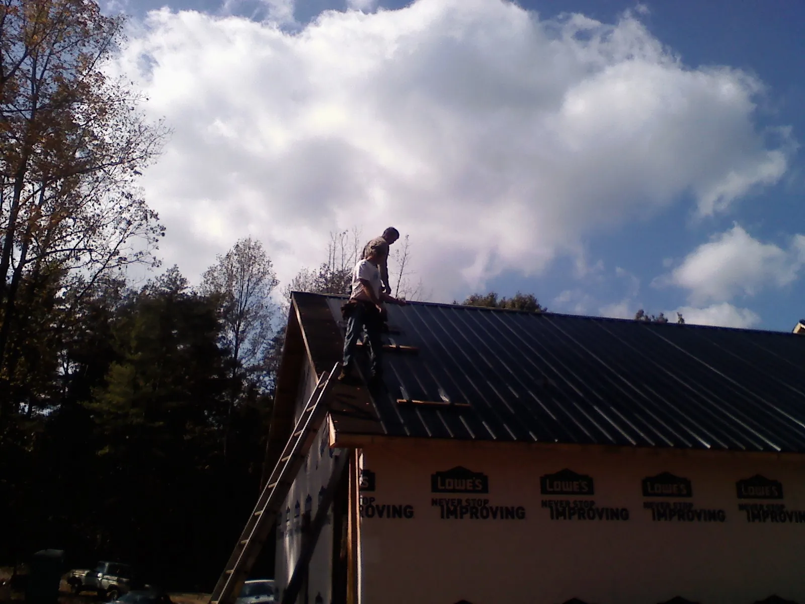 Roofer fastening dark metal panels high against a cloudy sky, from a Roof Inspection job in Wilton