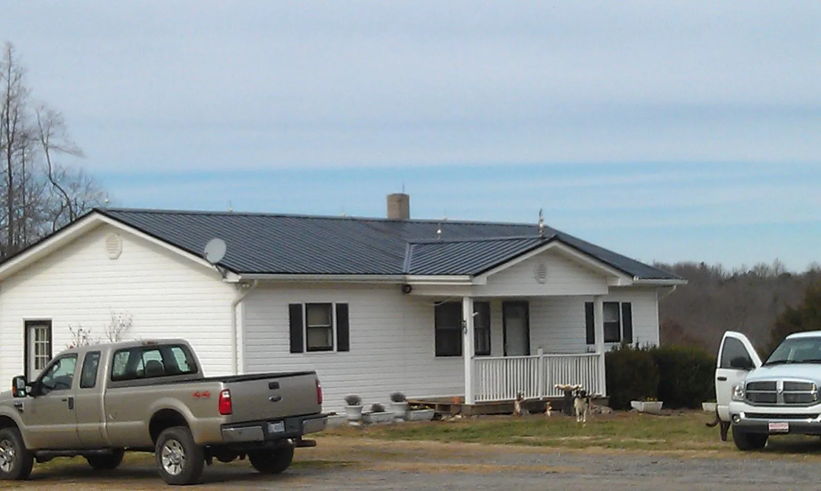 Finished dark metal roof on a white ranch home with work trucks parked in Wilton